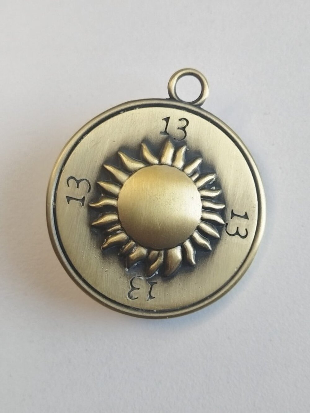 Antique brass pendant in the shape of a solar wheel, set with a green glass ston
